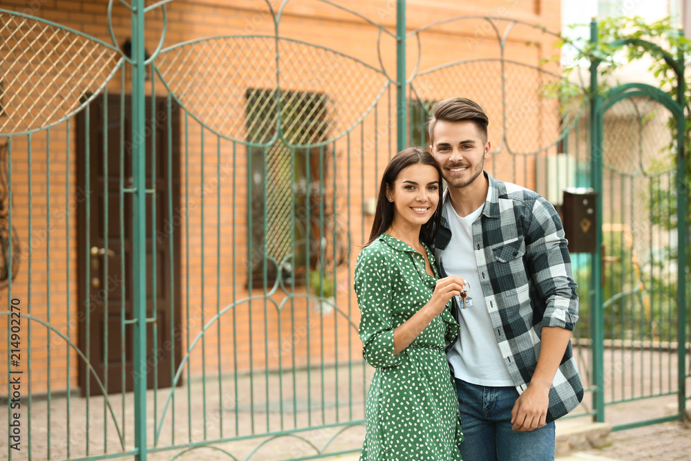 年轻幸福的夫妇，带着钥匙在户外新房子附近