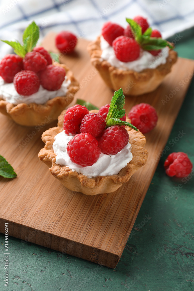 Tasty tartlets with raspberries on wooden board