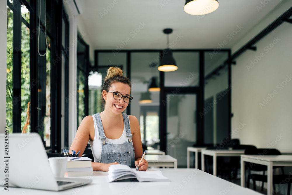 Portrait of a smiling millenial girl studying in modern study room.