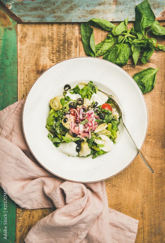 Flat-lay of fresh green summer salad with artichokes, olives, soft cheese and red onion in white pla