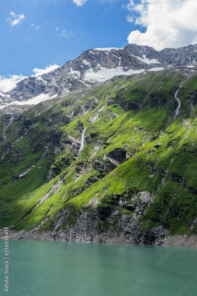 高山山峰、莫莱尼、冰川小溪和瀑布的景色。绿色的高山草甸带着黄色