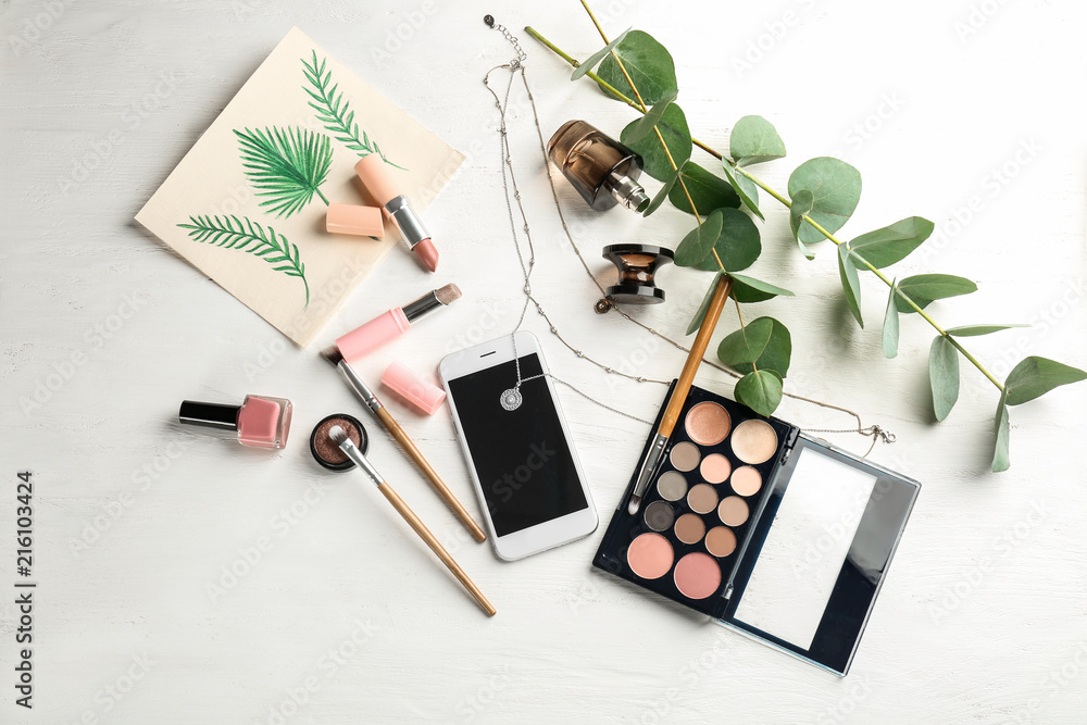 Composition with decorative cosmetics  and mobile phone on white wooden background