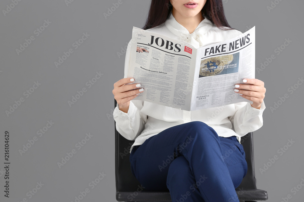 Young woman reading newspaper against grey background