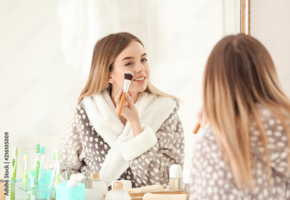 Beautiful young woman applying makeup in morning