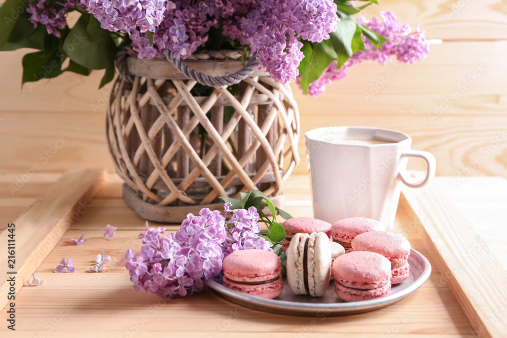 Plate with tasty macarons and beautiful blossoming lilac on table