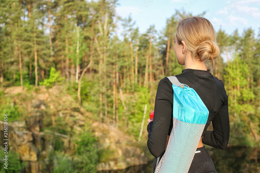 Beautiful young woman with yoga mat outdoors in morning