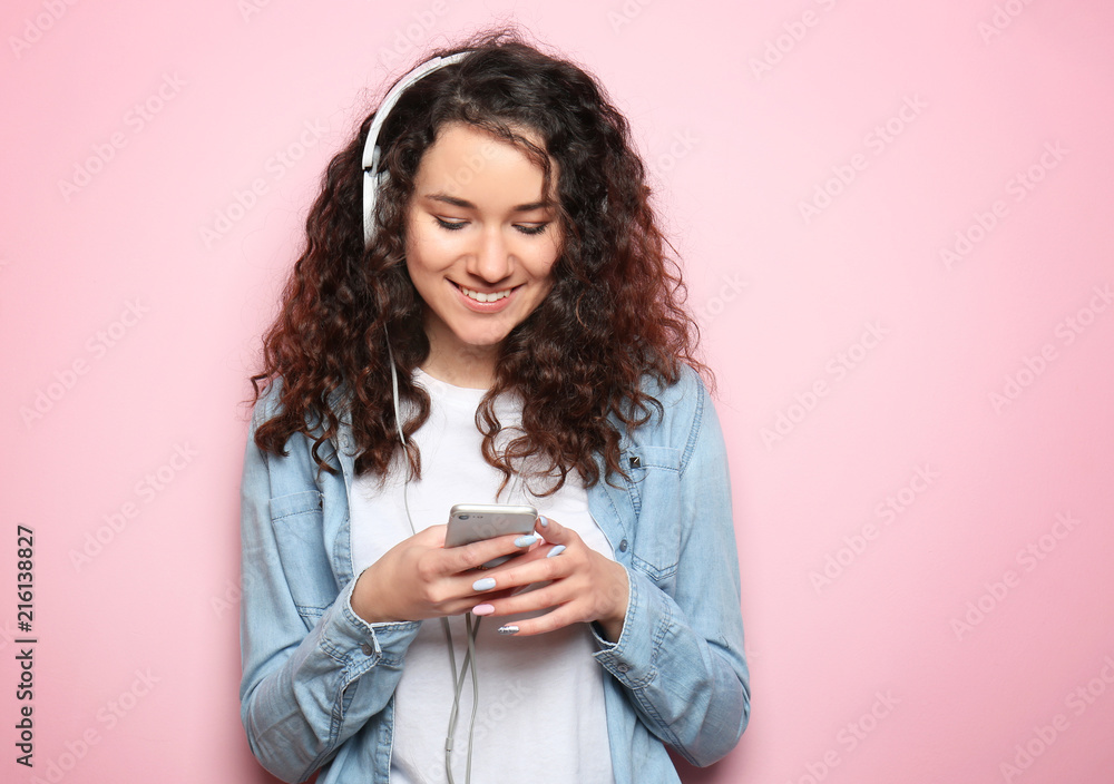 Portrait of young beautiful woman with smartphone and headphones on color background