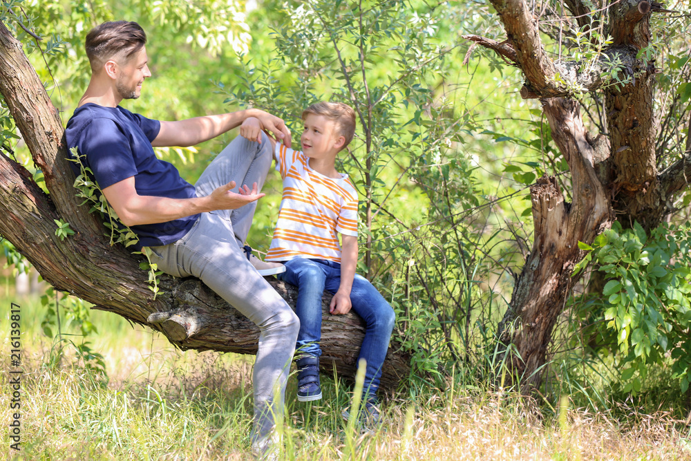 Little boy and his dad sitting on tree outdoors