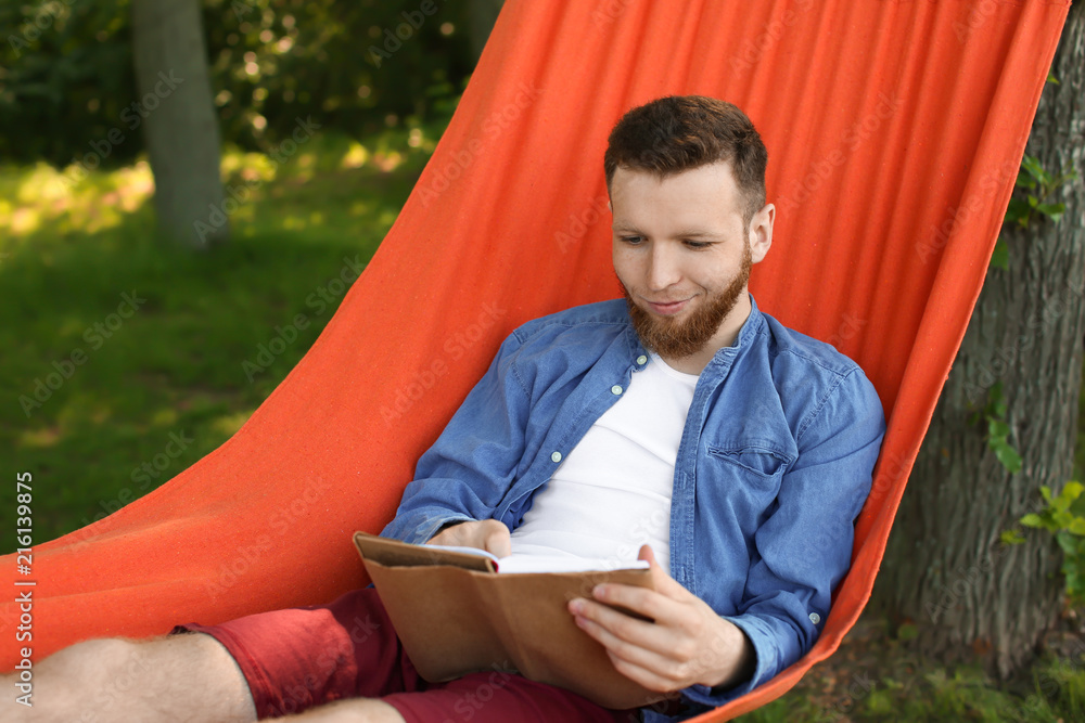 Young man reading book in hammock outdoors