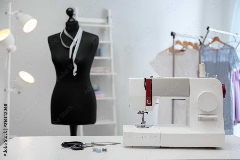 Modern sewing machine with tailors supplies on table in workshop