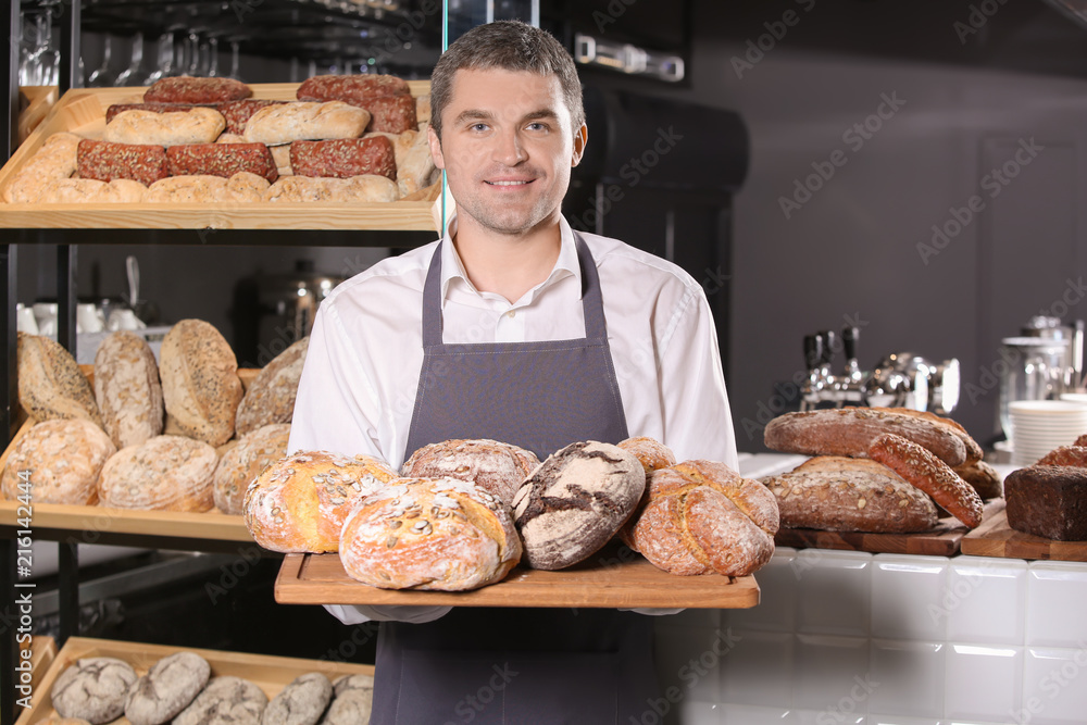 Man holding board with assortment of fresh bread in bakery