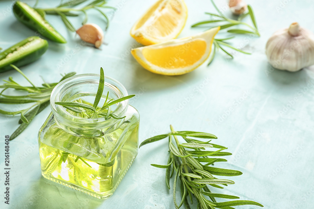 Glass jar with oil and fresh rosemary on table