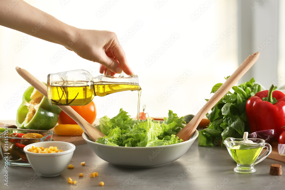 Woman adding olive oil to fresh vegetable salad on table