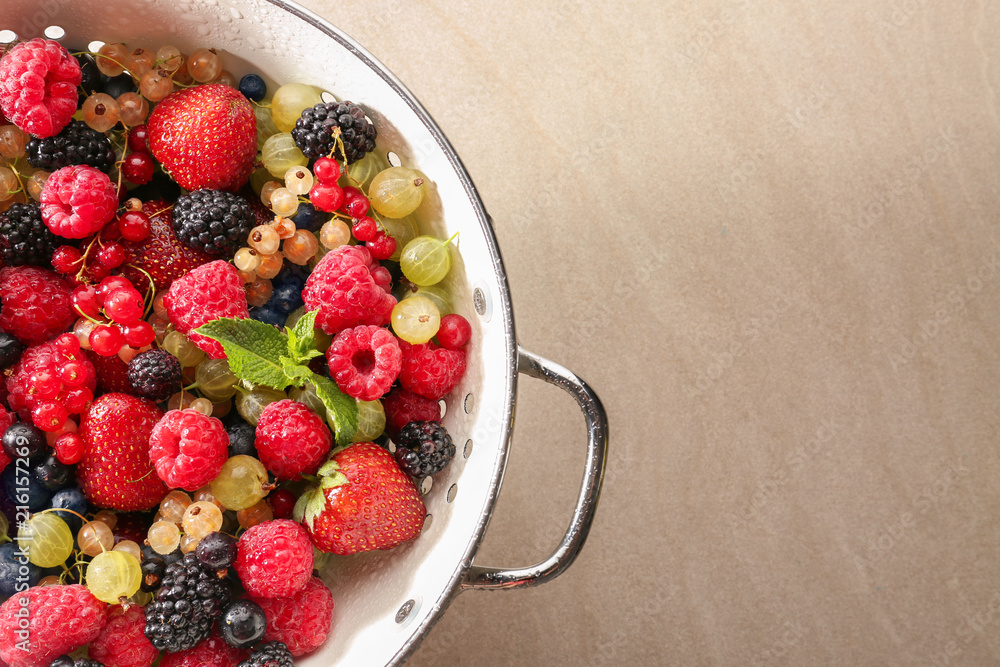 Colander with fresh ripe berries on light table