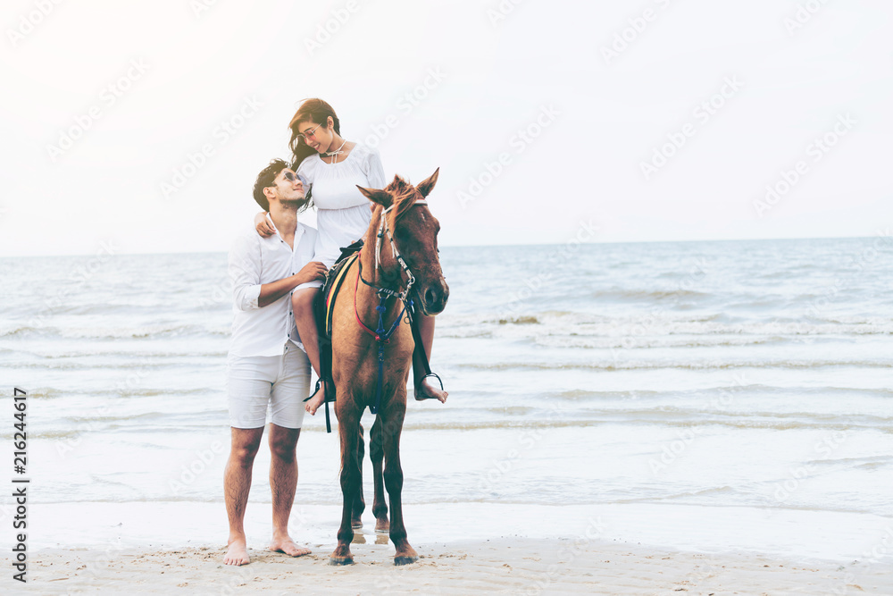 一对年轻夫妇在热带海滩上骑马。