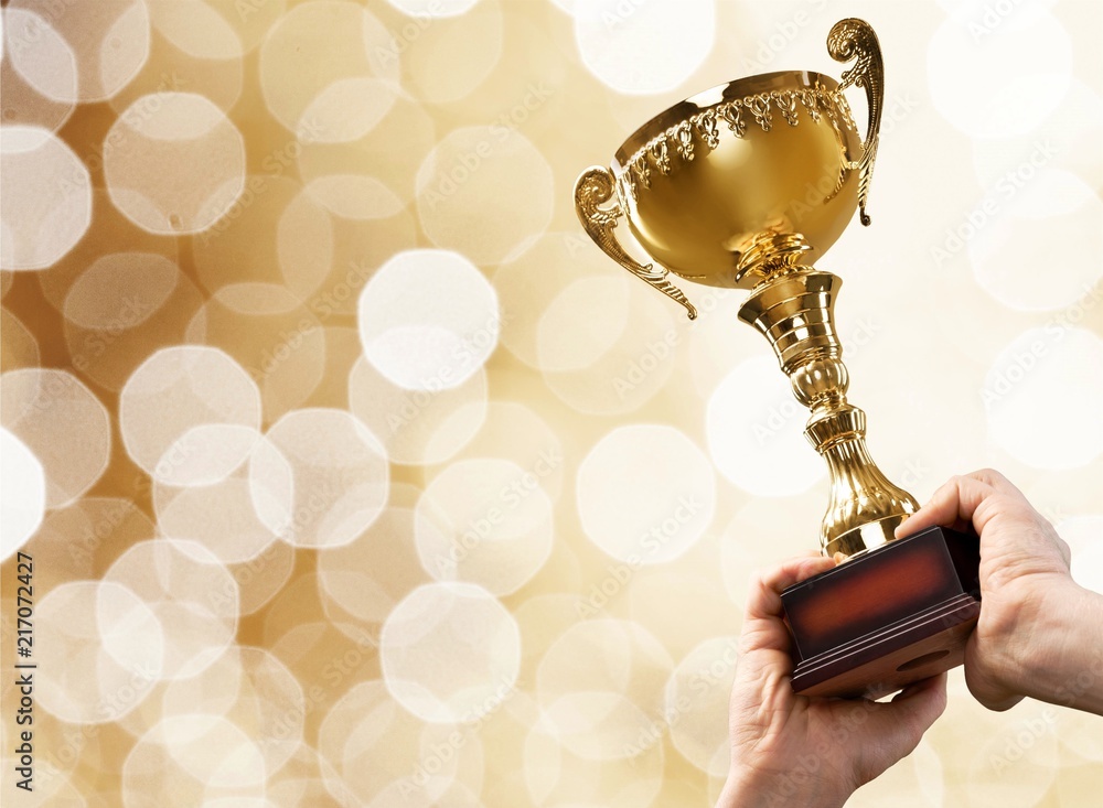 Hands holding golden trophy on light background