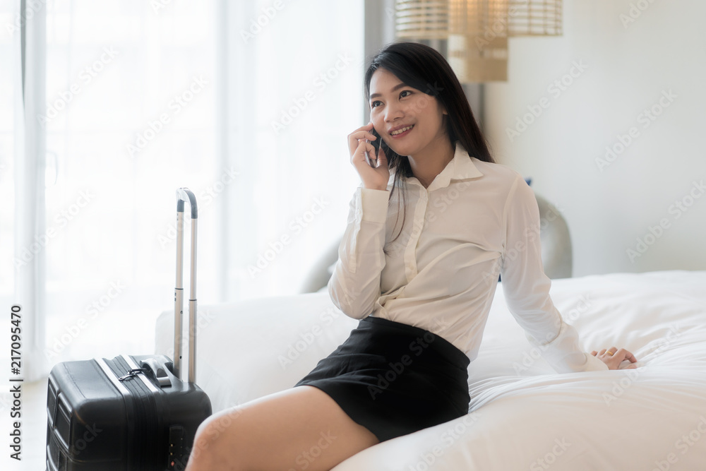 Beautiful Asian young smiling businesswoman in suit drinking coffee and using mobile phone while sit