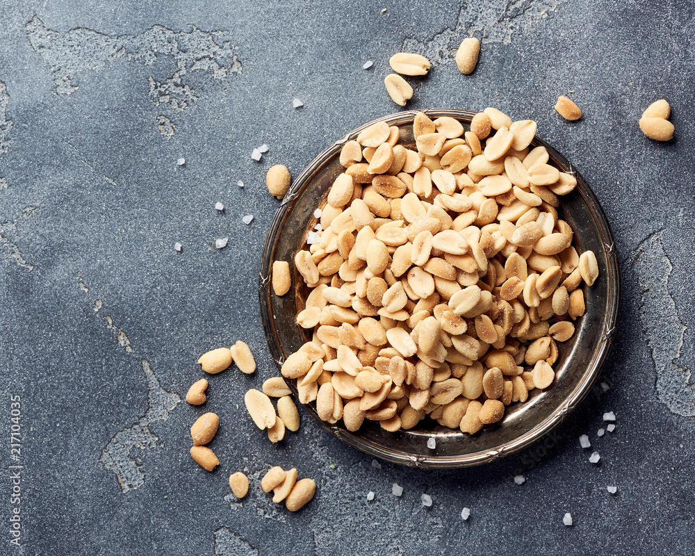 Salted roasted peanuts seeds on plate over gray concrete background.