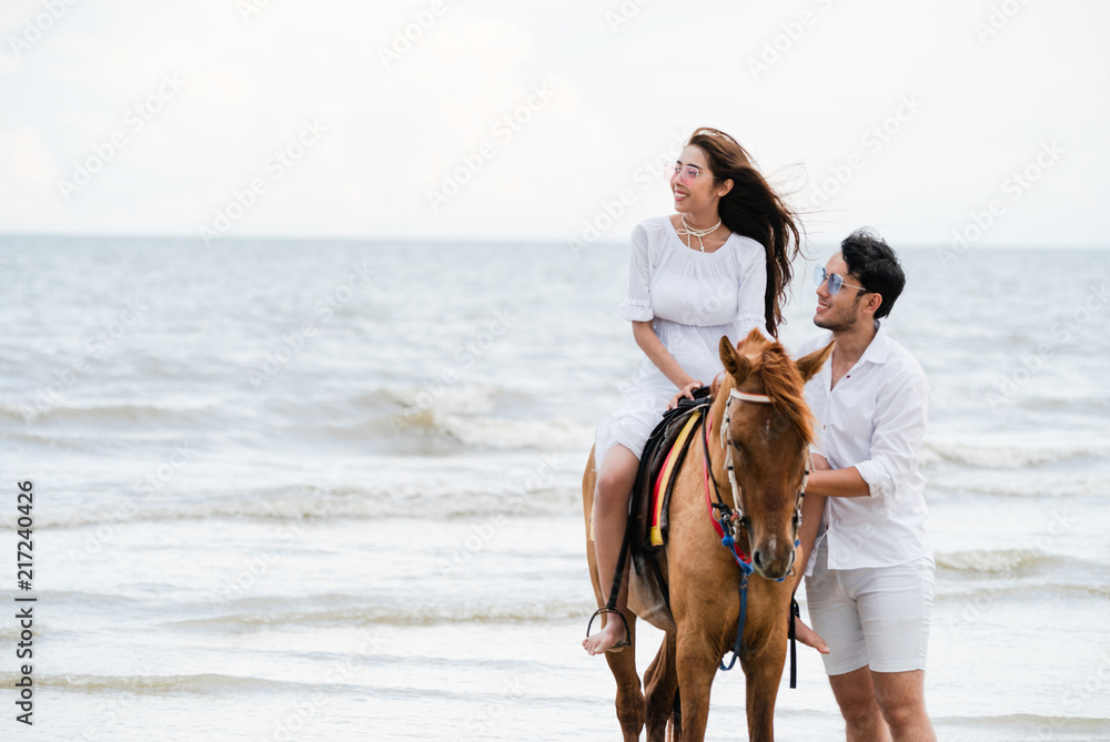 一对年轻夫妇在热带海滩上骑马。