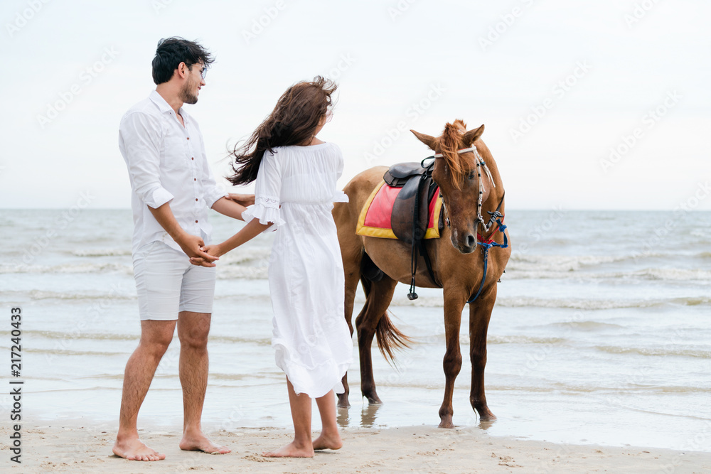 一对年轻夫妇在热带海滩上骑马。