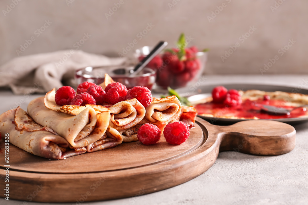 Board with tasty thin pancakes and berries on light table, closeup