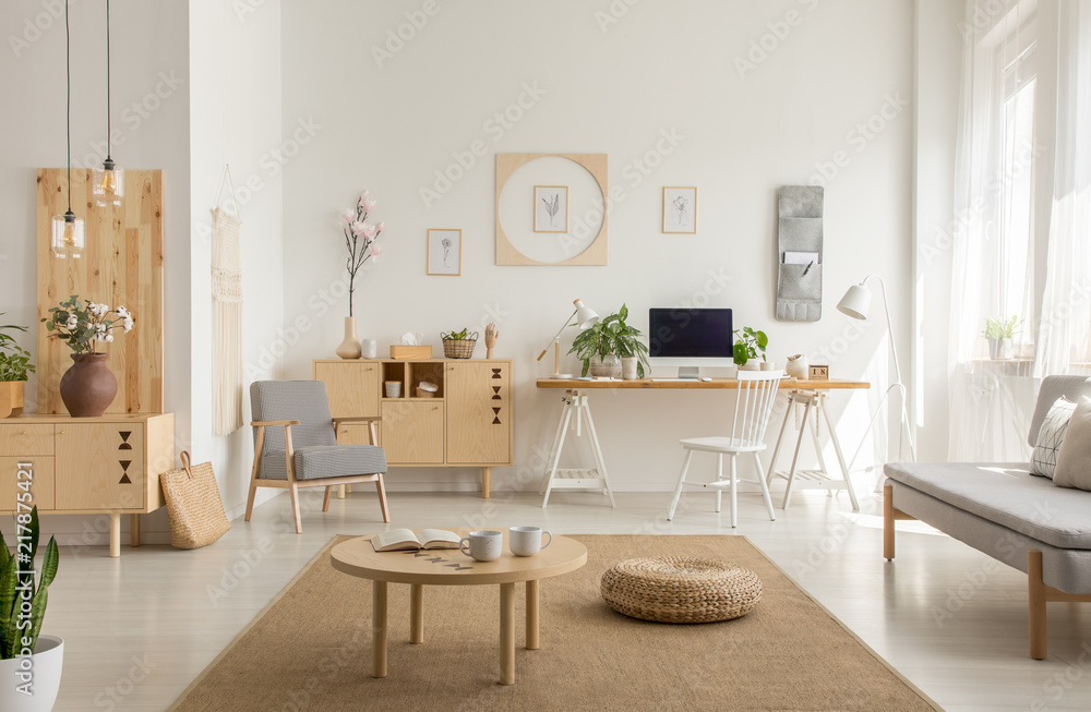 Wooden table and pouf on carpet in white living room interior with poster and workspace. Real photo