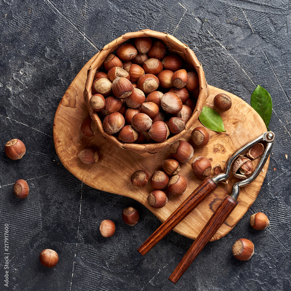 Hazelnut with nutcracker on olive wooden board. Nuts with green leaves. Top view.