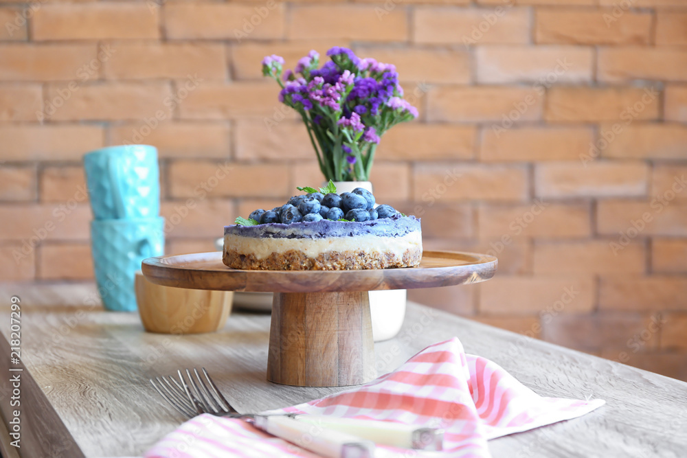 Stand with tasty blueberry cheesecake and flowers on wooden table