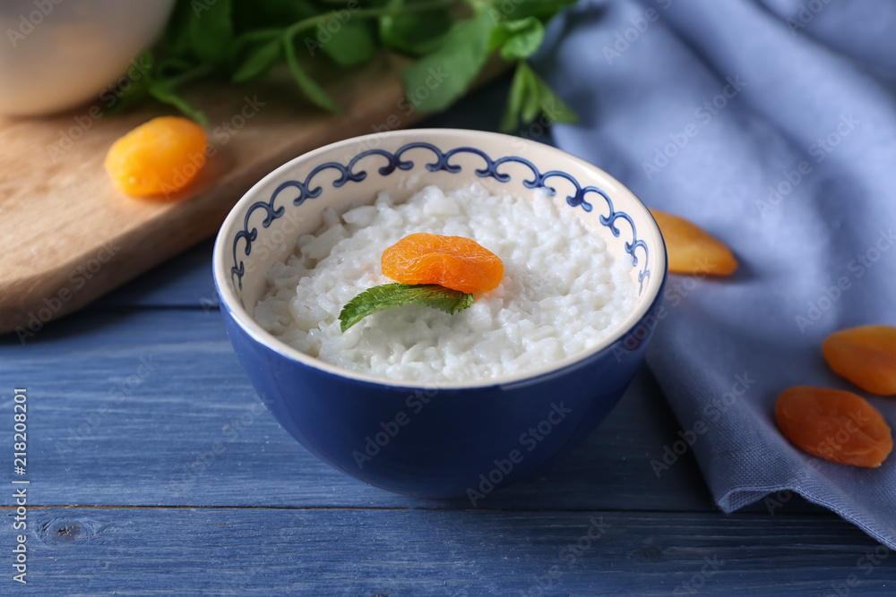 Bowl with delicious rice pudding and dried apricot on wooden table