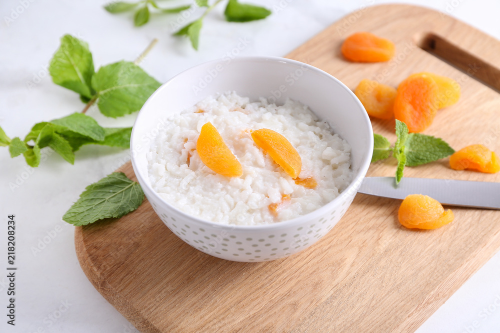 Bowl with delicious rice pudding and dried apricot on board