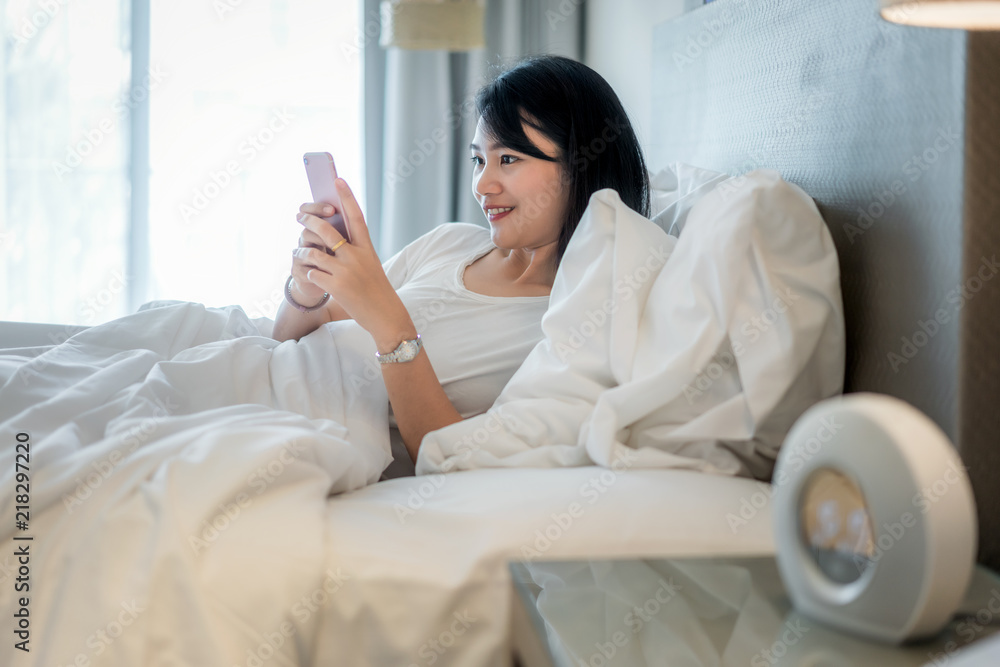 Morning with gadget. Asian beautiful young woman lying on the bed using smartphone. .