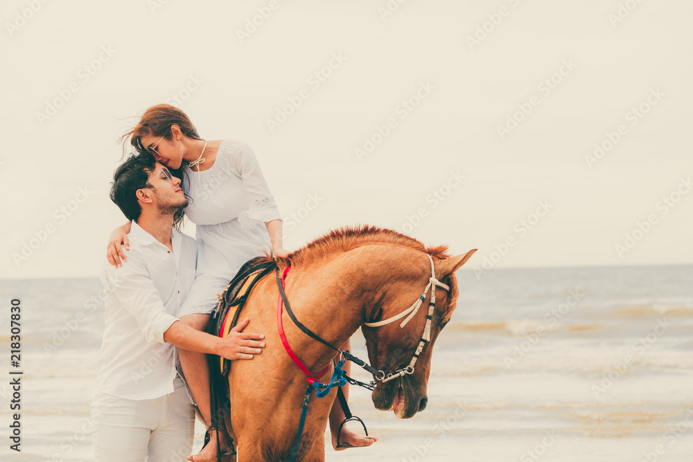 一对年轻夫妇在热带海滩上骑马。