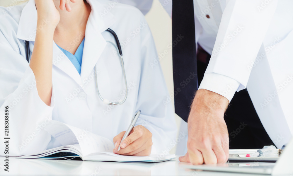 Doctor writes report at desk with another doctor.