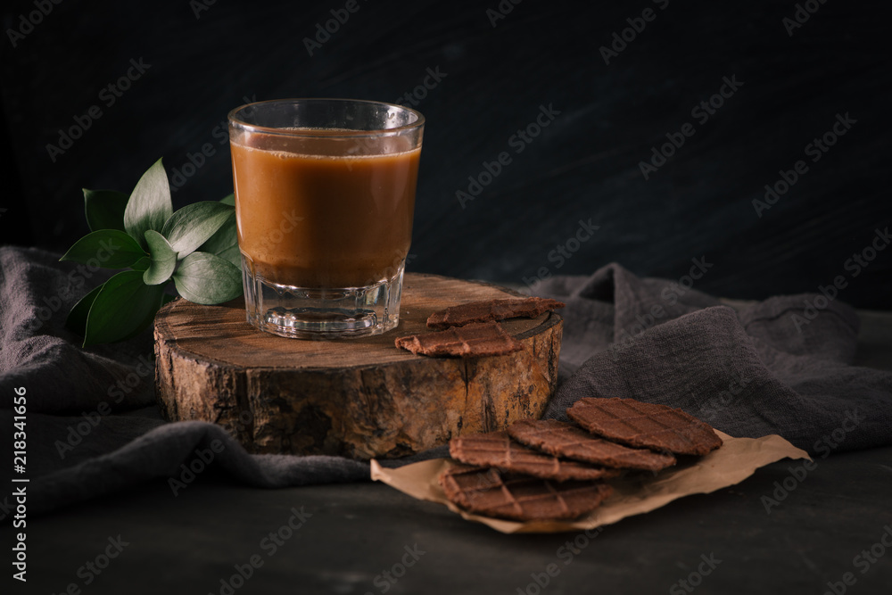 Assorted cookies in brown paper and glass of coffee with milk on dark background.