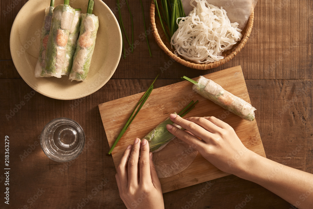 Fresh spring rolls with shrimps with cooker hands on background