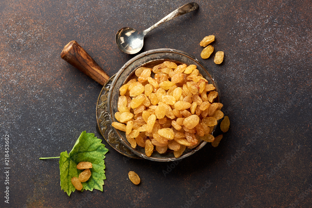 Heap of yellow raisins. Top view of dried grapes with green leaf.