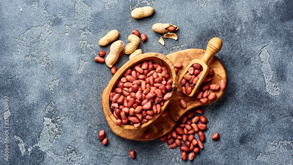 Peeled peanuts in bowl and scoop on gray background. Top view of nuts.