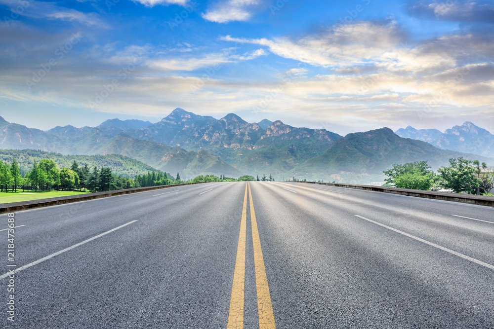 Straight asphalt highway and green mountain nature landscape at sunset