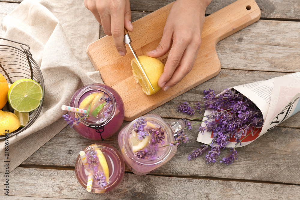 Young woman preparing lavender lemonade at wooden table, closeup