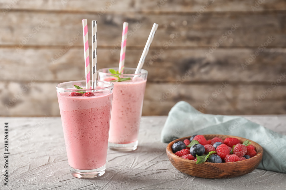 Glasses with tasty raspberry smoothie and berries on light table