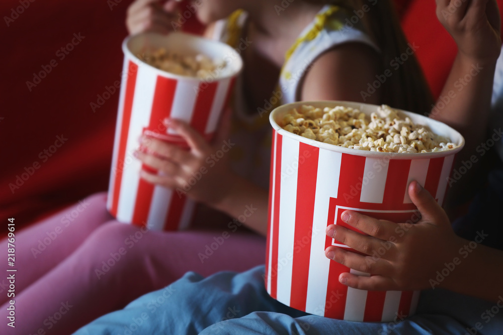 Cute children eating popcorn while watching TV in evening