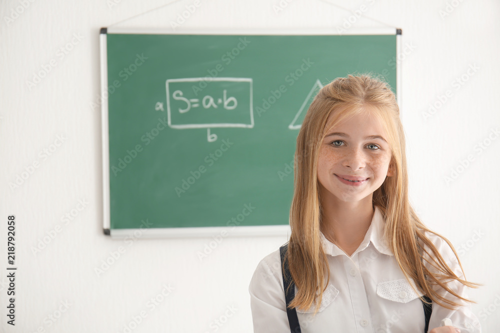 Cute schoolgirl near chalkboard in classroom