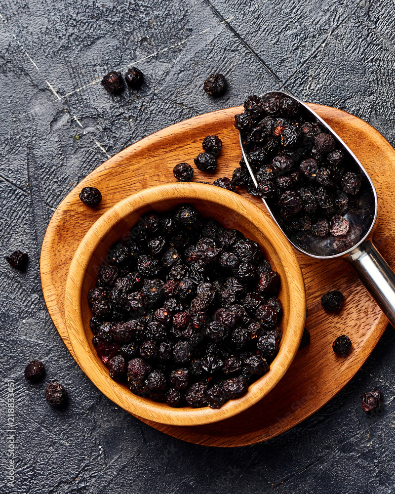 Dried cherry in wooden bowl on black background. Top view of berries.