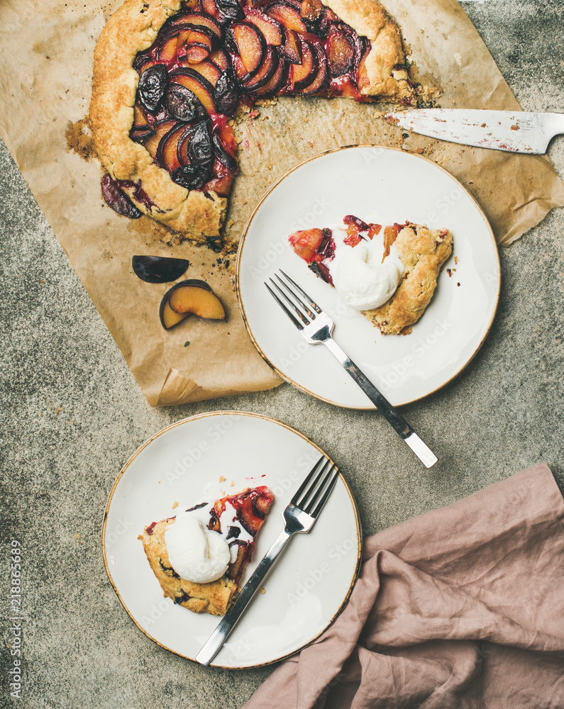 Flat-lay of plum galetta sweet cake in white plates over grey concrete background, top view. Seasona