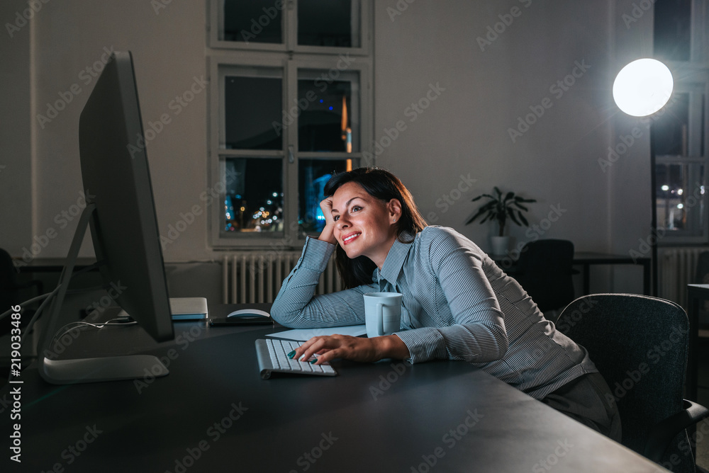 Happy young businesswoman working late at night.