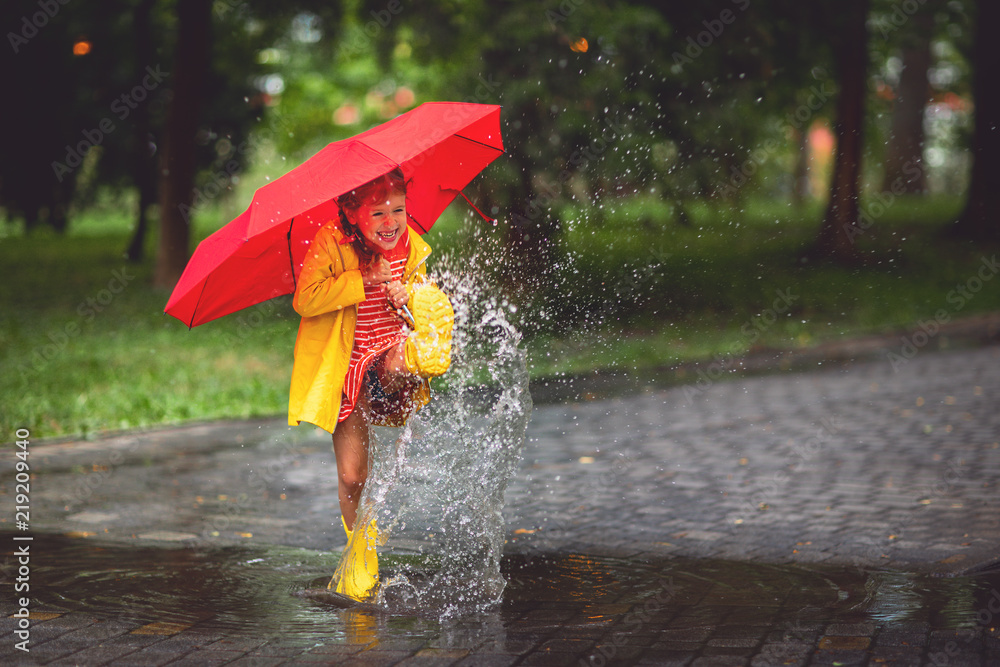 快乐的小女孩，带着雨伞和橡胶靴在水坑里秋天散步