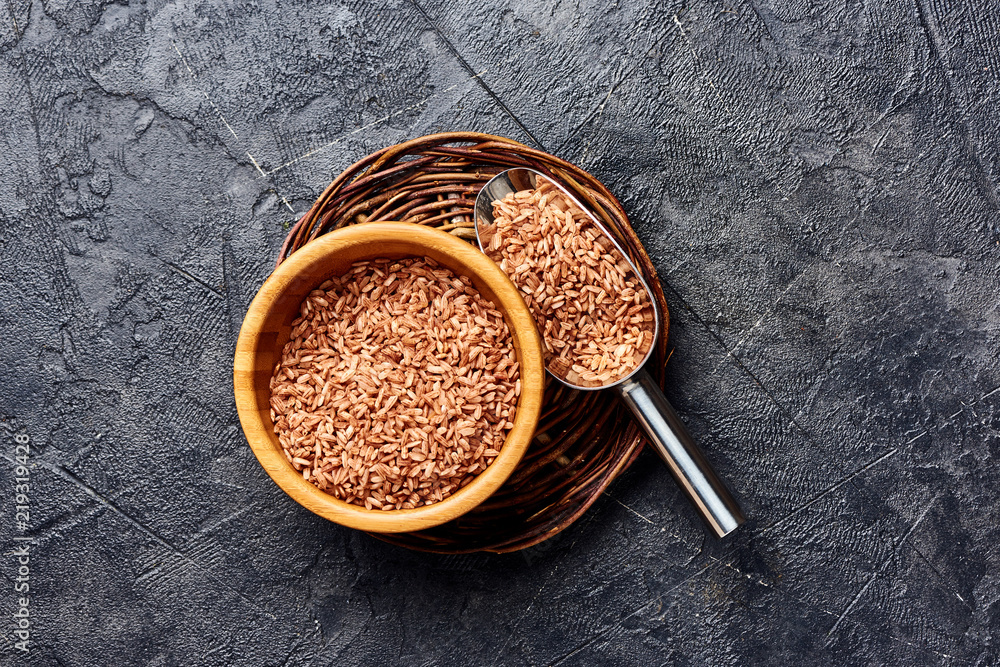 Wild brown rice in wooden bowl on black background. Top view of grains.