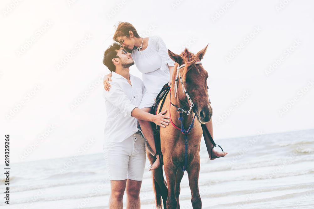 Young couple goes horse riding on tropical beach.