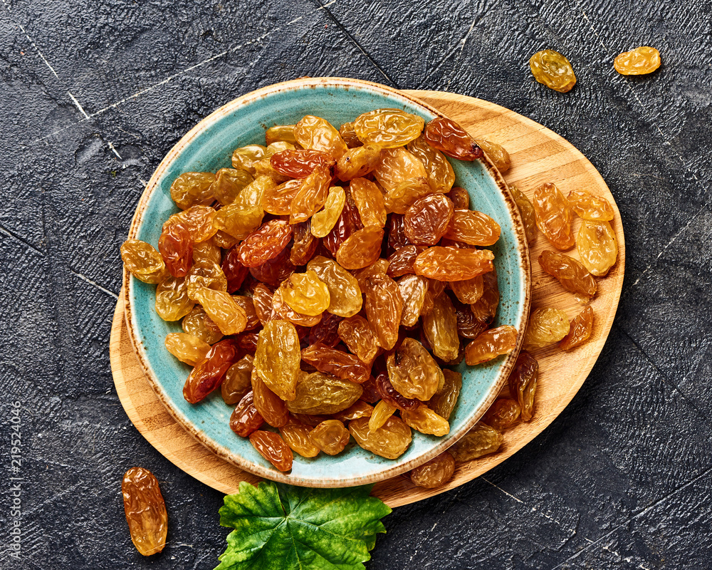 Yellow big raisins on black concrete background. Top view of dried grapes.