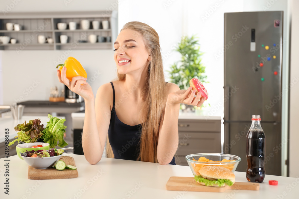 年轻女性在厨房里选择甜甜圈和胡椒。减肥食品概念